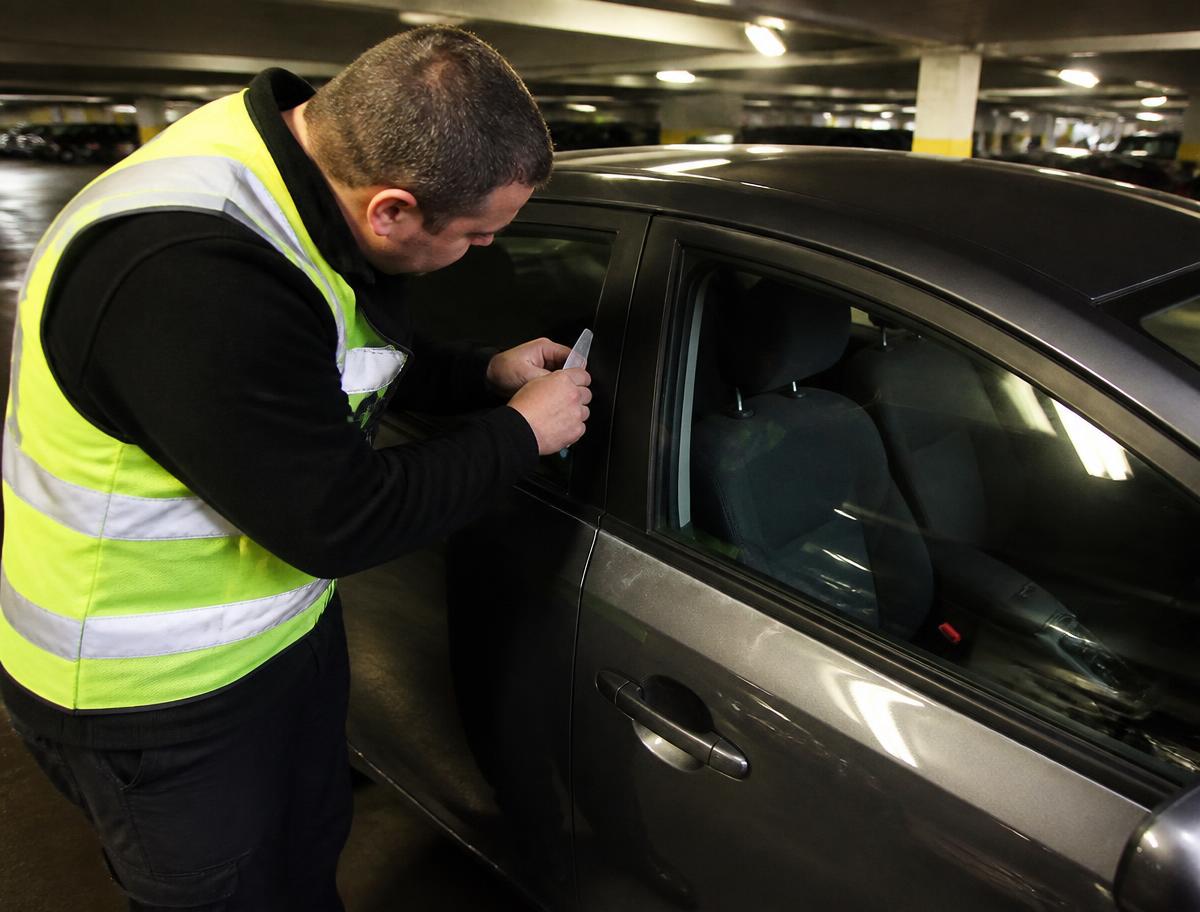 Technician using a slim entry tool at a locked car door in a parking garage
